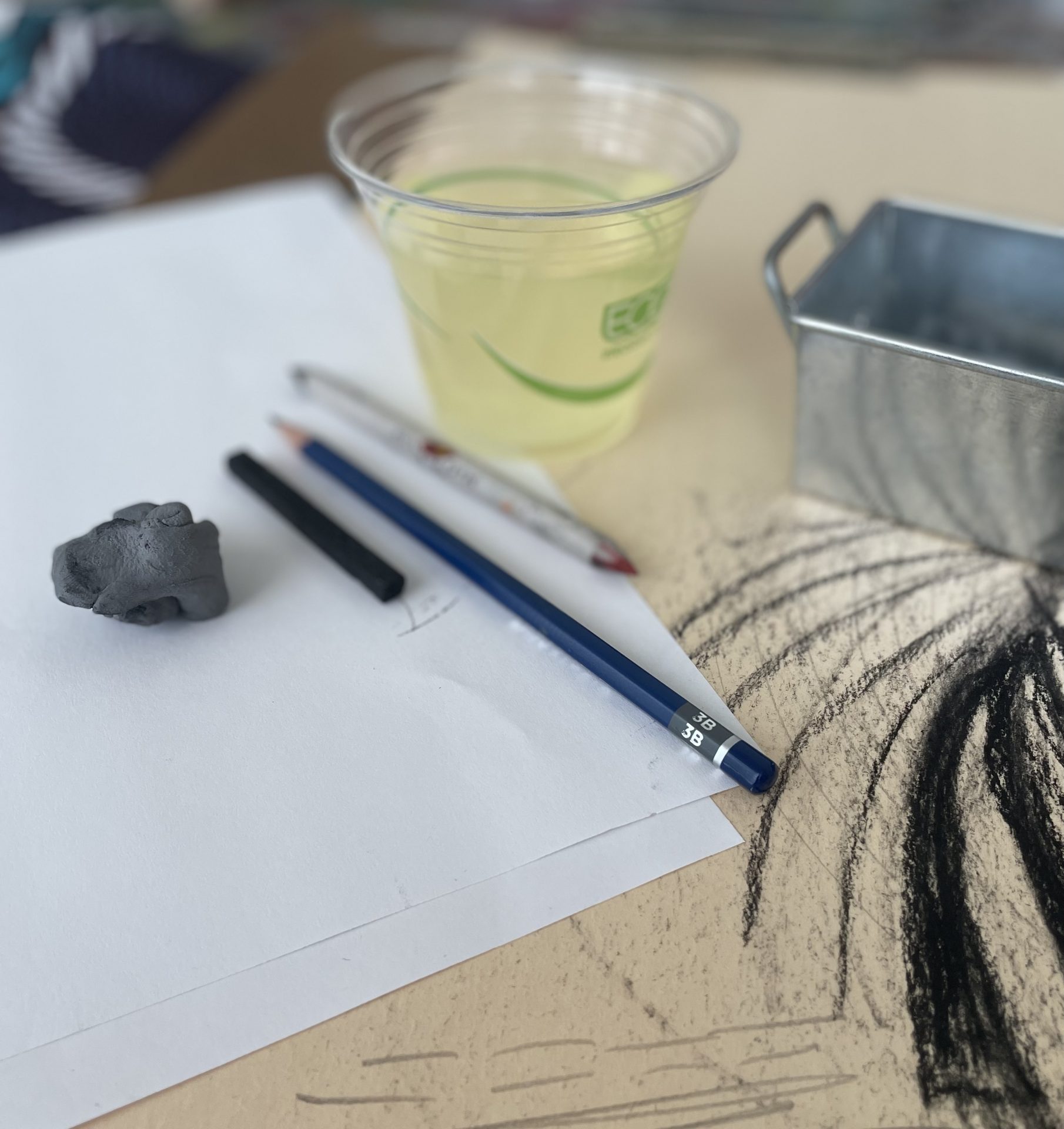 A disposable class filled with white wine sits on a table with drawing materials