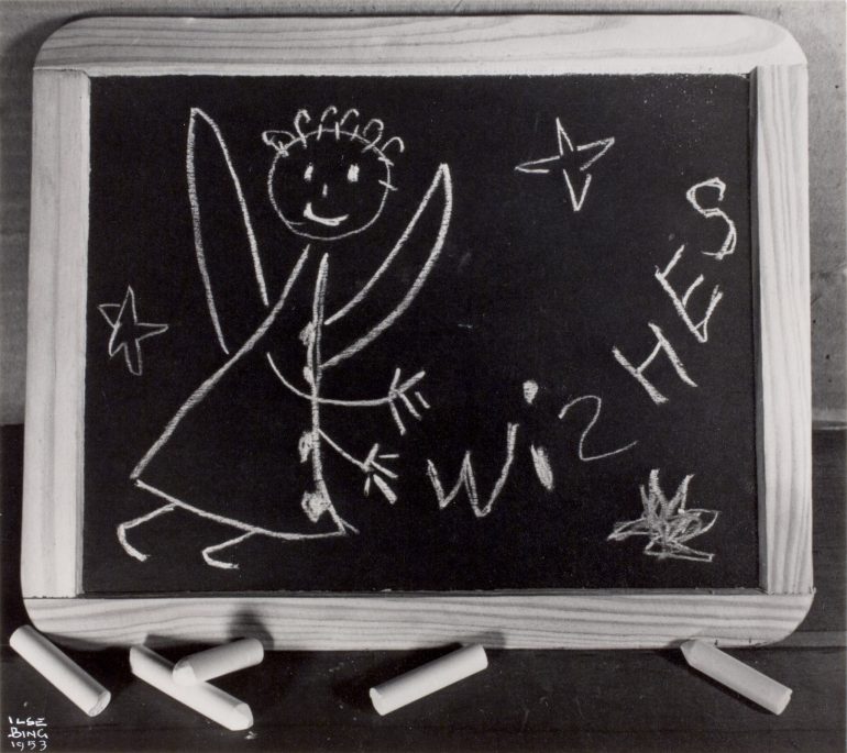 A black and white photograph of a handheld chalkboard shows a handdrawn angel with the word "WISHES"