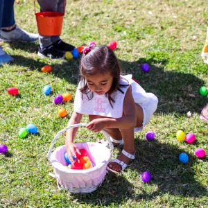 A child stoops on the ground to pick up plastic Easter eggs and put them in a basket